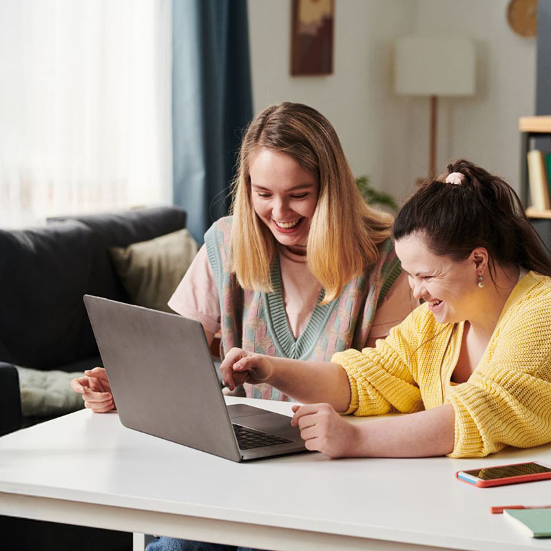 Zwei Frauen schauen auf einen Laptop und lachen